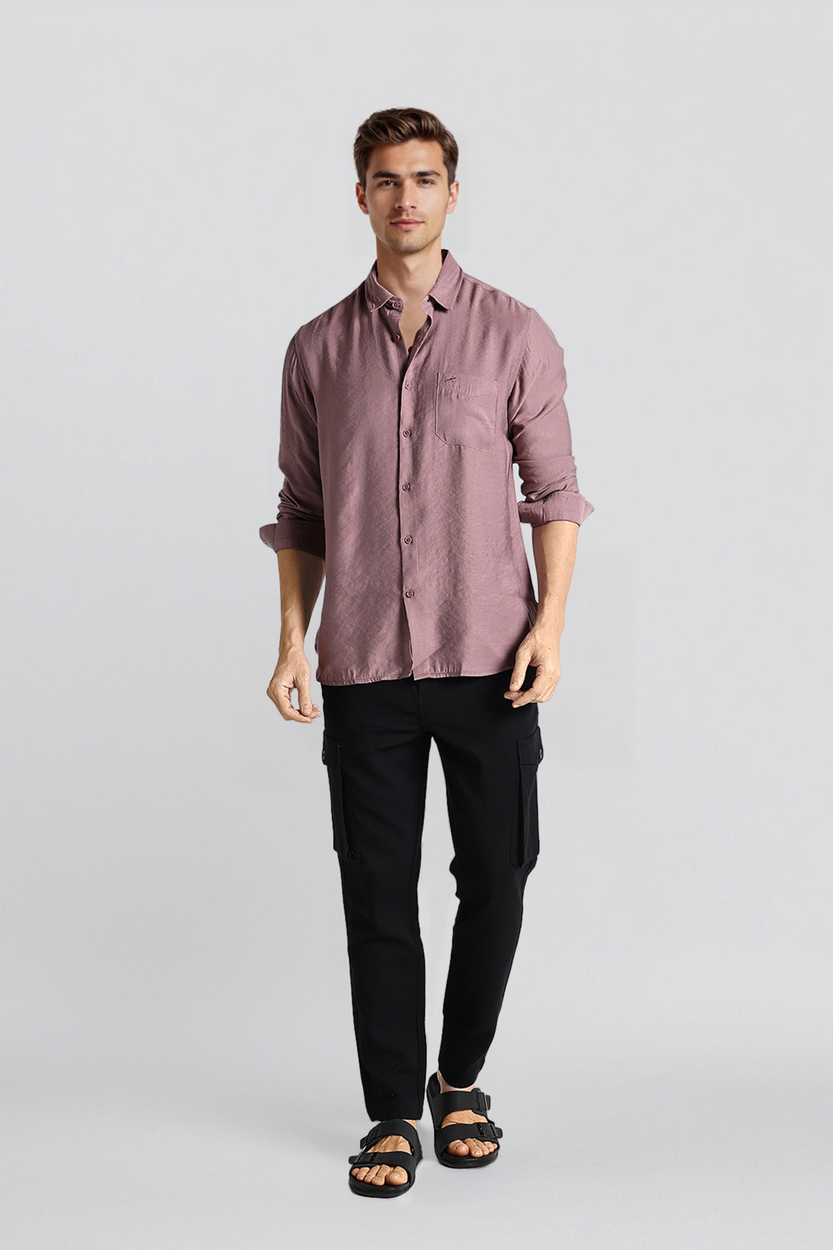 Man wearing a mauve button-up shirt and black pants on a light gray background