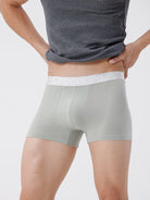 Person wearing light gray boxer briefs with a visible brand logo on a plain background