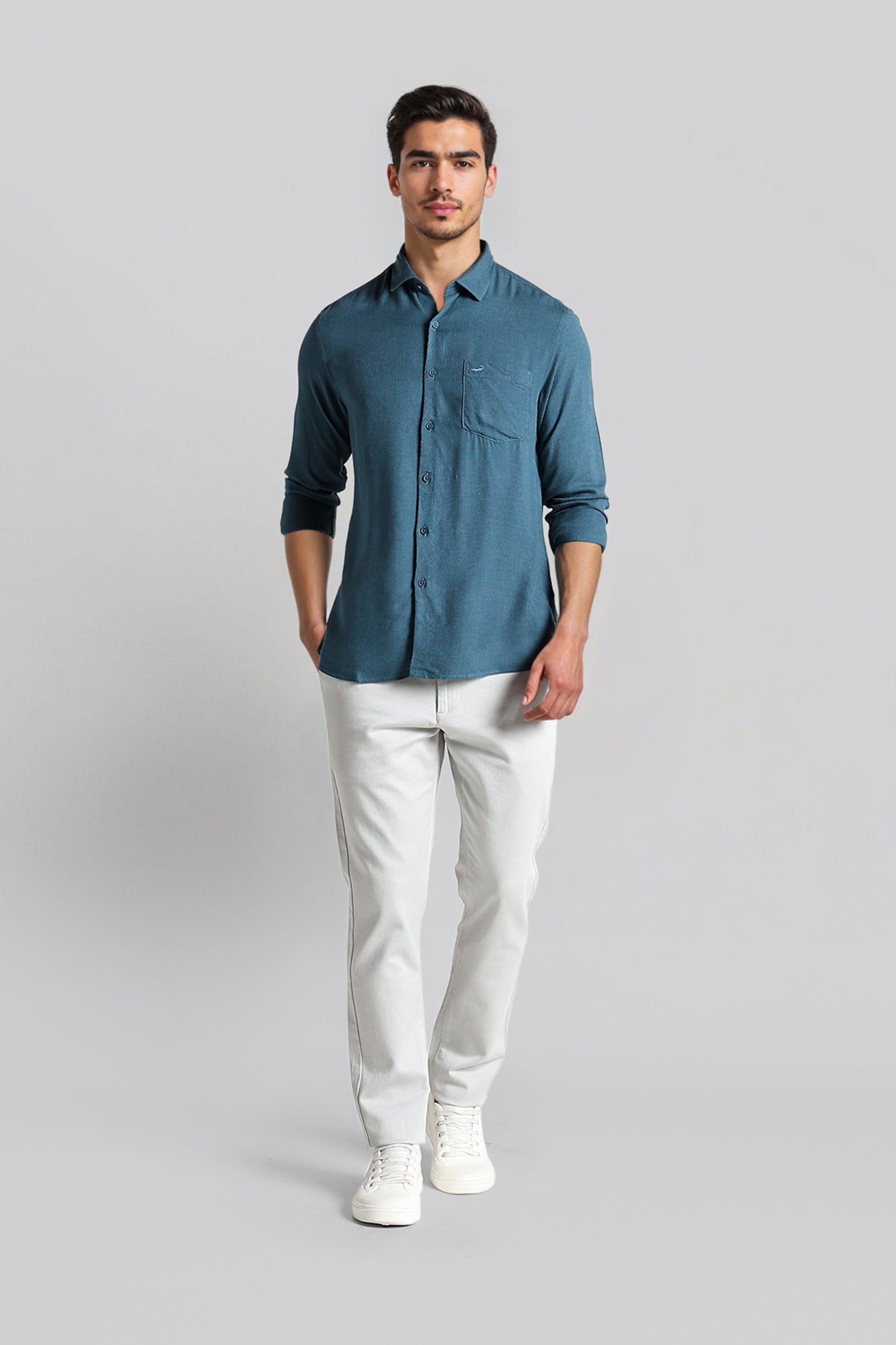 Man wearing a blue shirt and white pants on a gray background