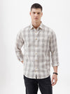 A man wearing a long-sleeve button-up plaid shirt in beige, white, and gray, paired with dark pants, standing against a plain white studio background.
