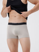 Person wearing beige boxer briefs with a black waistband on a white background