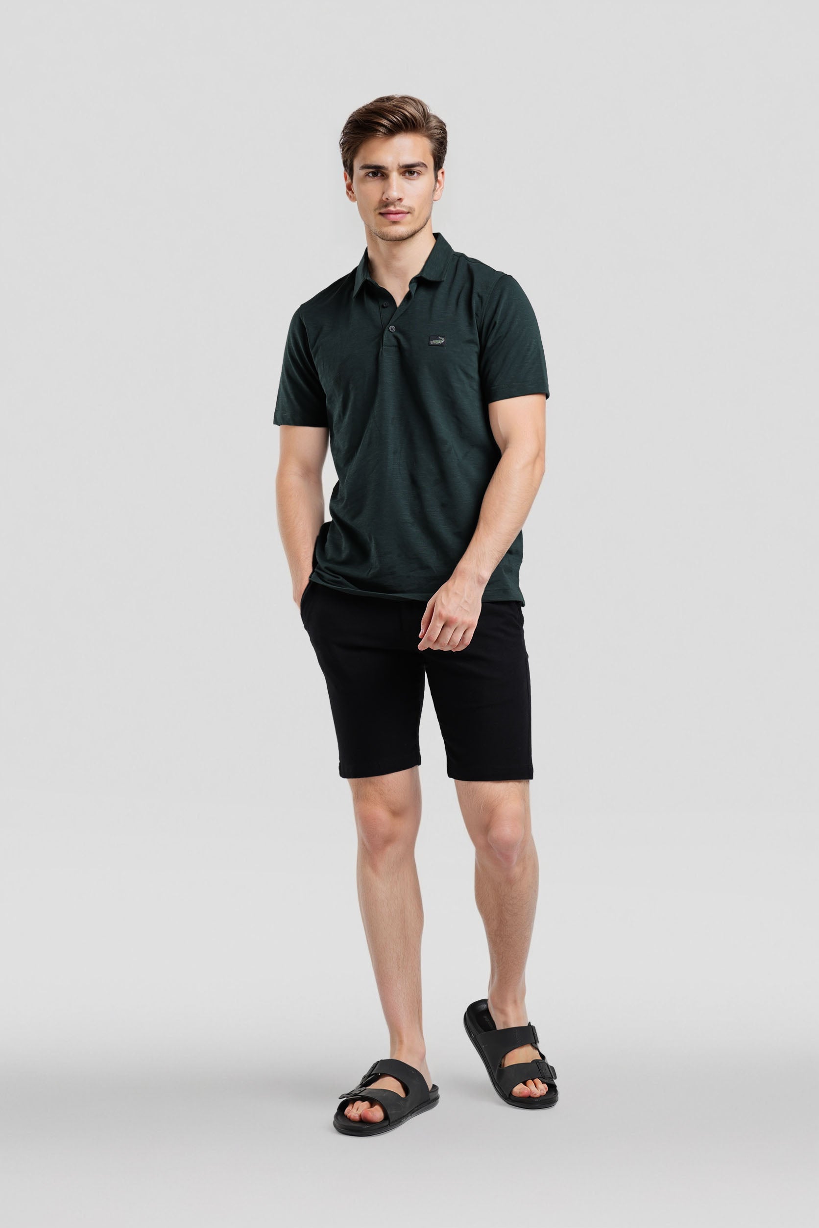 Man wearing a dark green polo shirt and black shorts on a light gray background
