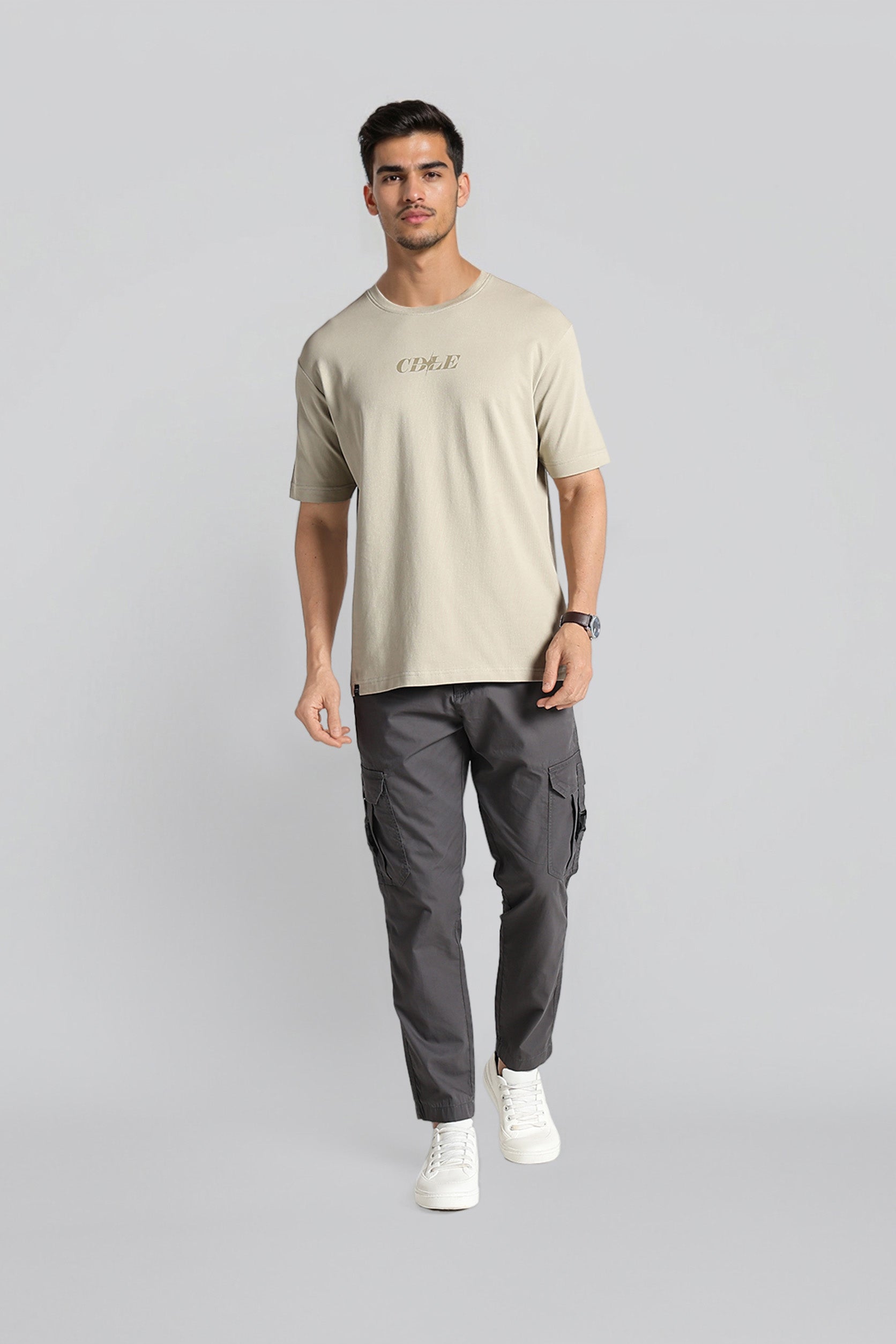 Man wearing a beige t-shirt and gray cargo pants on a light gray background