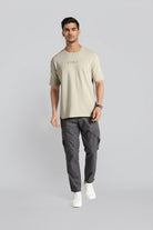 Man wearing a beige t-shirt and gray cargo pants on a light gray background