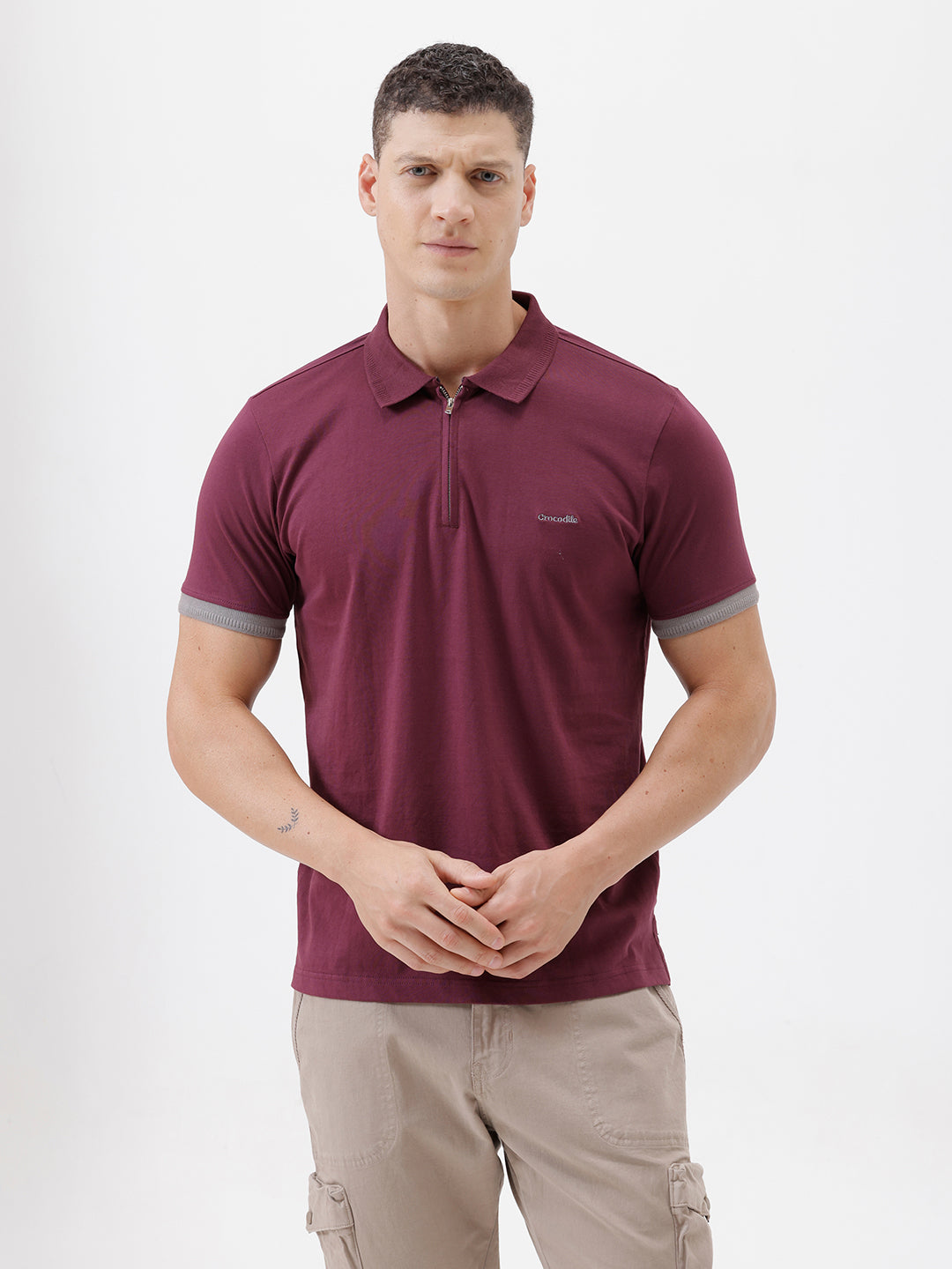 A man wearing a short-sleeve polo shirt in maroon with gray sleeve trim and a half-zip collar, paired with beige cargo pants, against a plain white studio background.