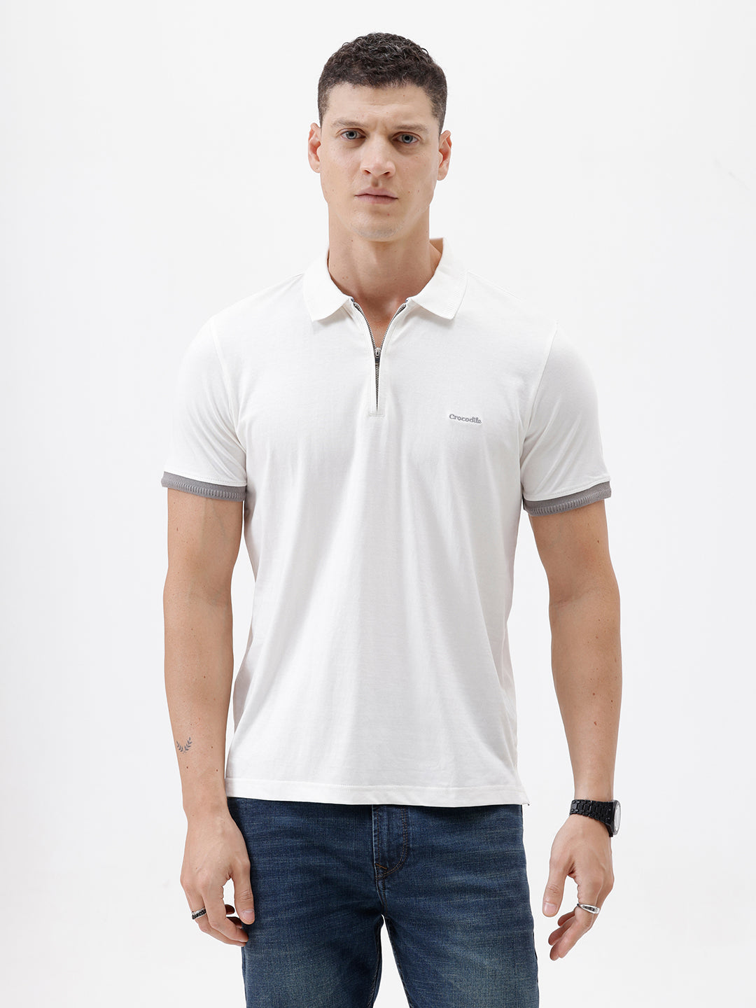 A man wearing a white short-sleeve polo shirt with gray ribbed trim on the collar and sleeve cuffs, paired with dark blue jeans, photographed against a plain white studio background.
