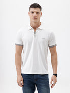 A man wearing a white short-sleeve polo shirt with gray ribbed trim on the collar and sleeve cuffs, paired with dark blue jeans, photographed against a plain white studio background.