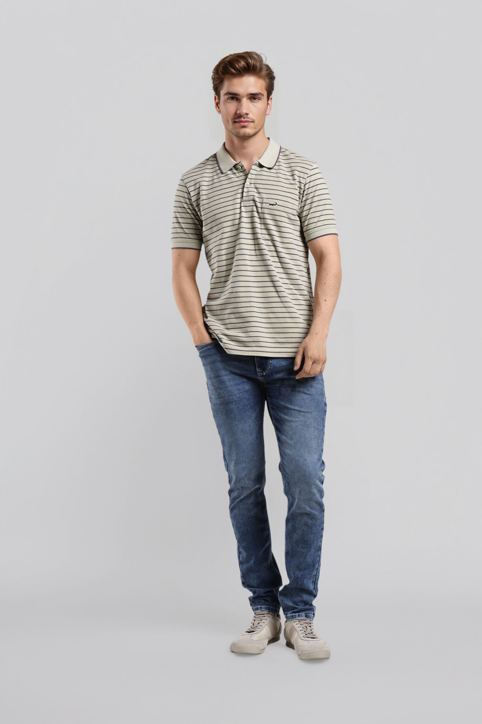 Man wearing a striped polo shirt and blue jeans on a gray background