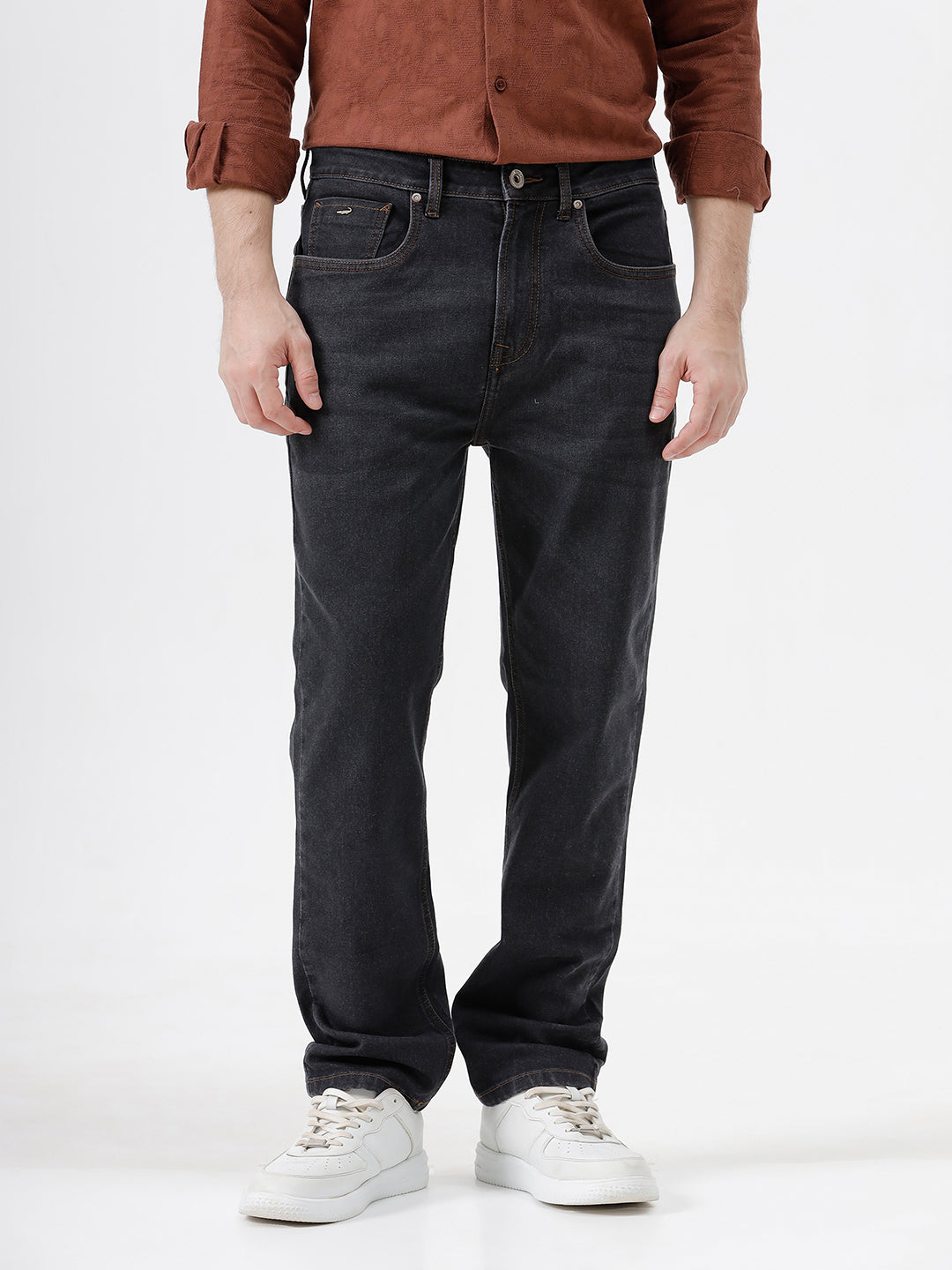 A person wearing dark charcoal gray slim-fit jeans, a rust-brown long-sleeve button-up shirt, and white sneakers, standing against a plain white studio background.