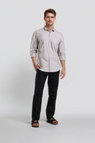 Man wearing a light gray button-up shirt and black pants on a white background