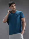 Man wearing a blue teal blue solid t shirt with casual styling on a gray background