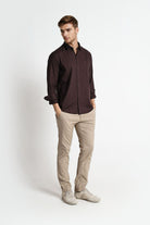 Man wearing a dark brown shirt and beige pants on a white background