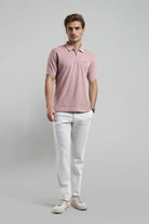 Man wearing a pink patterned polo shirt and white pants on a gray background