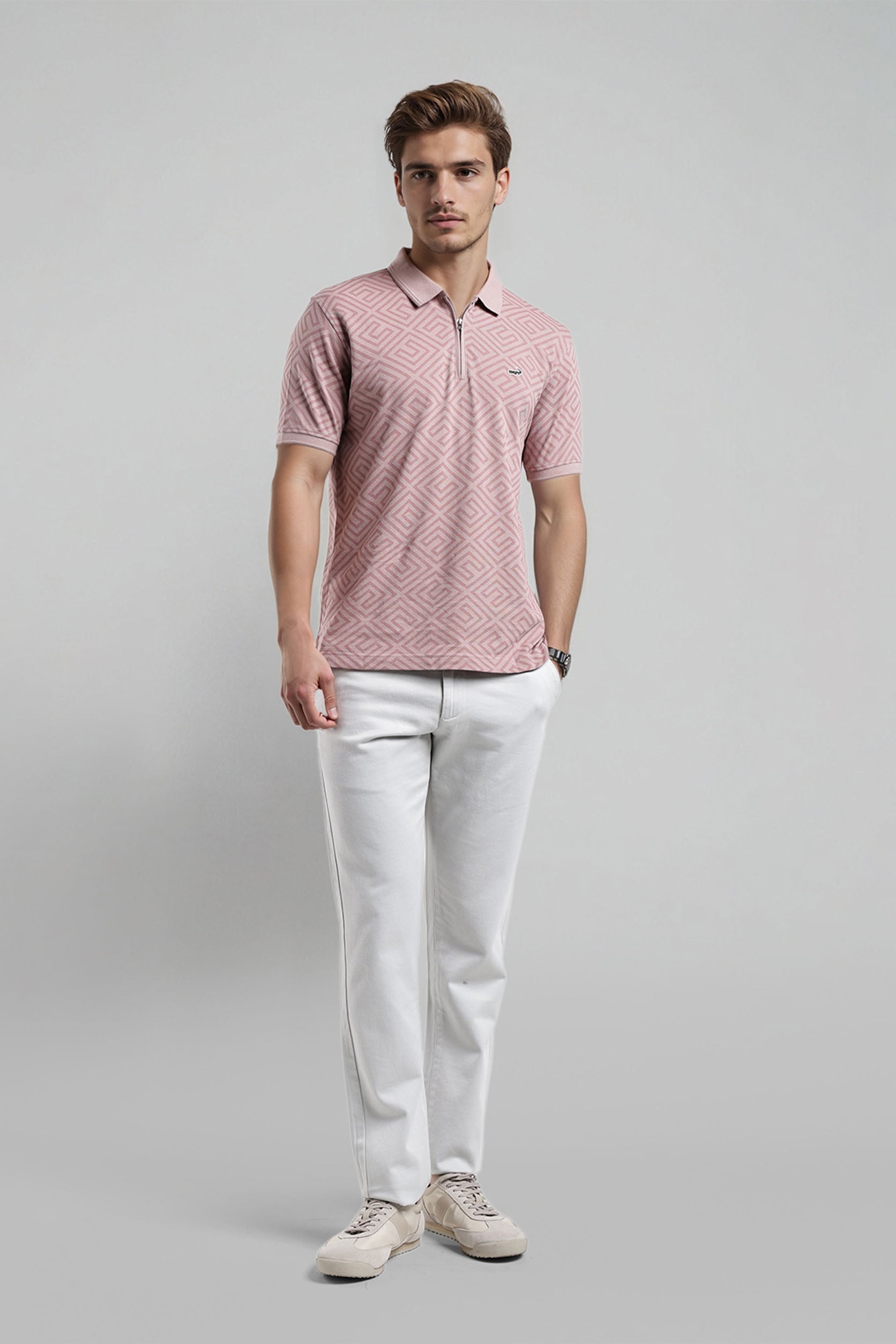 Man wearing a pink patterned polo shirt and white pants on a gray background