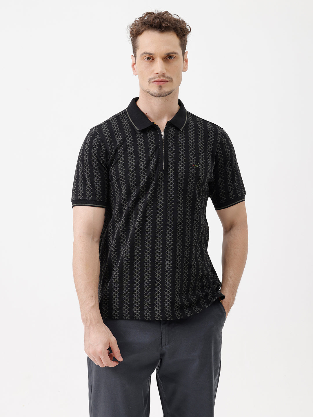 A man wearing a black short-sleeve polo shirt with a subtle geometric pattern, paired with dark gray trousers, standing against a plain white studio background.