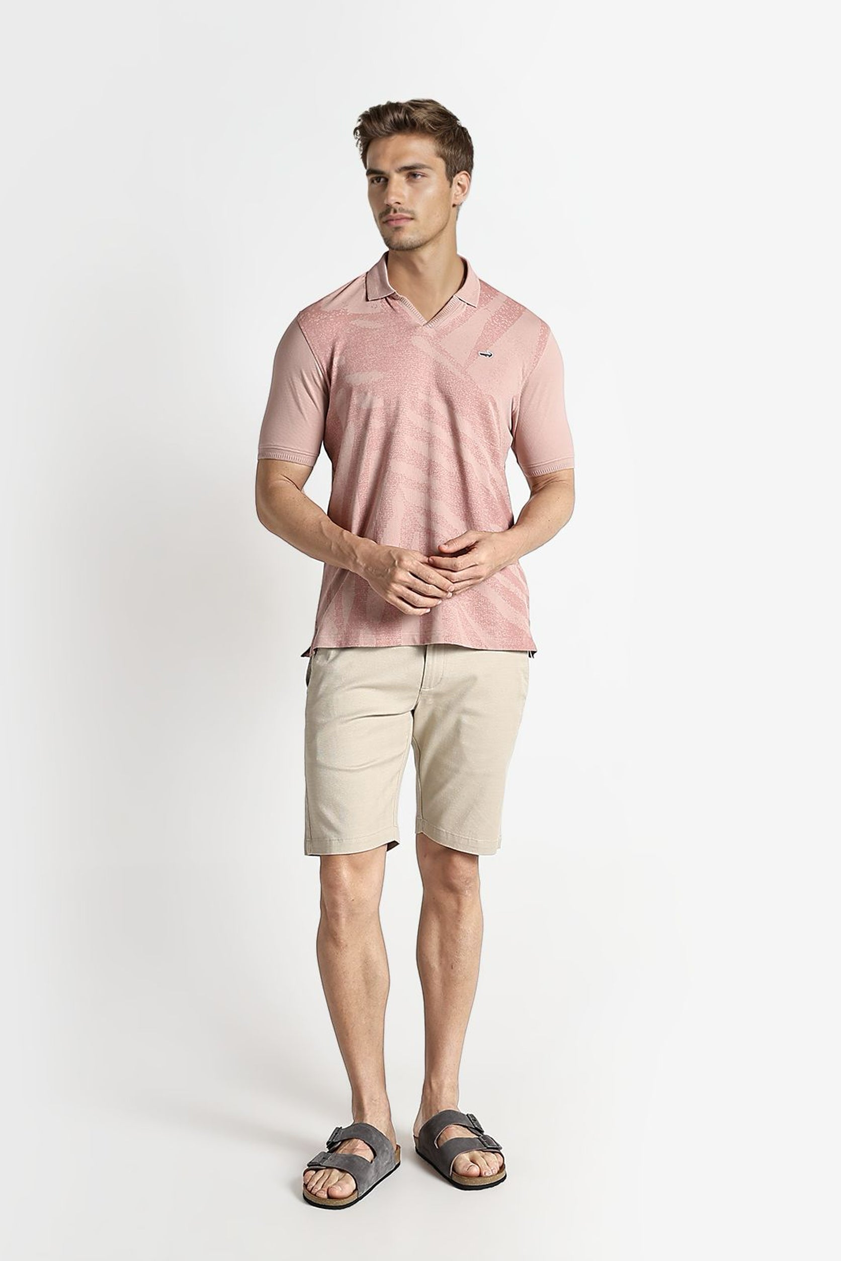 Man wearing a pink polo shirt and beige shorts on a white background