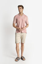 Man wearing a pink polo shirt and beige shorts on a white background