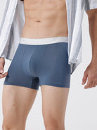Man wearing a pair of blue boxer briefs with a white label on a light gray background