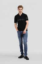 Man wearing a black polo shirt and blue jeans on a white background