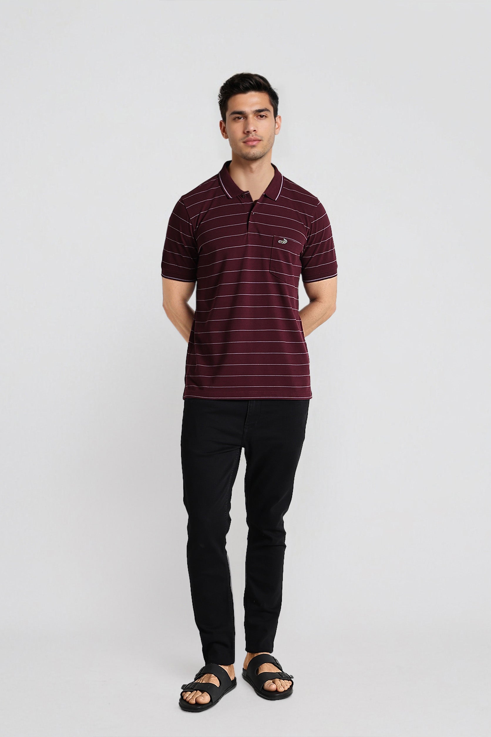 Man wearing a maroon striped polo shirt and black pants on a white background