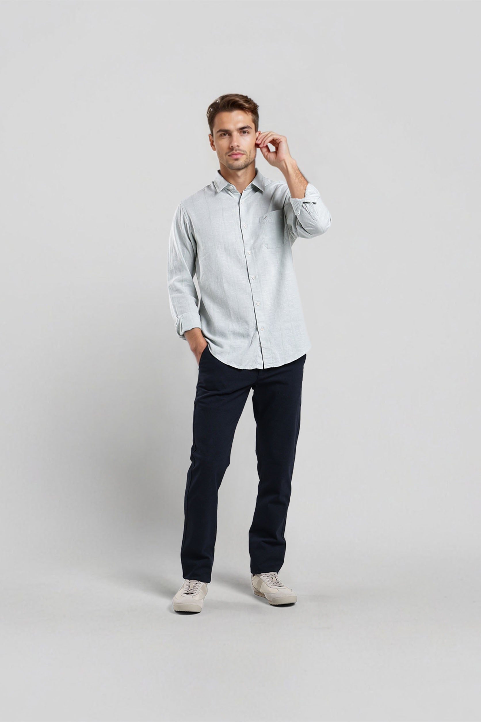 Man wearing a light gray button-up shirt and dark pants on a white background