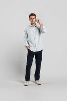 Man wearing a light gray button-up shirt and dark pants on a white background