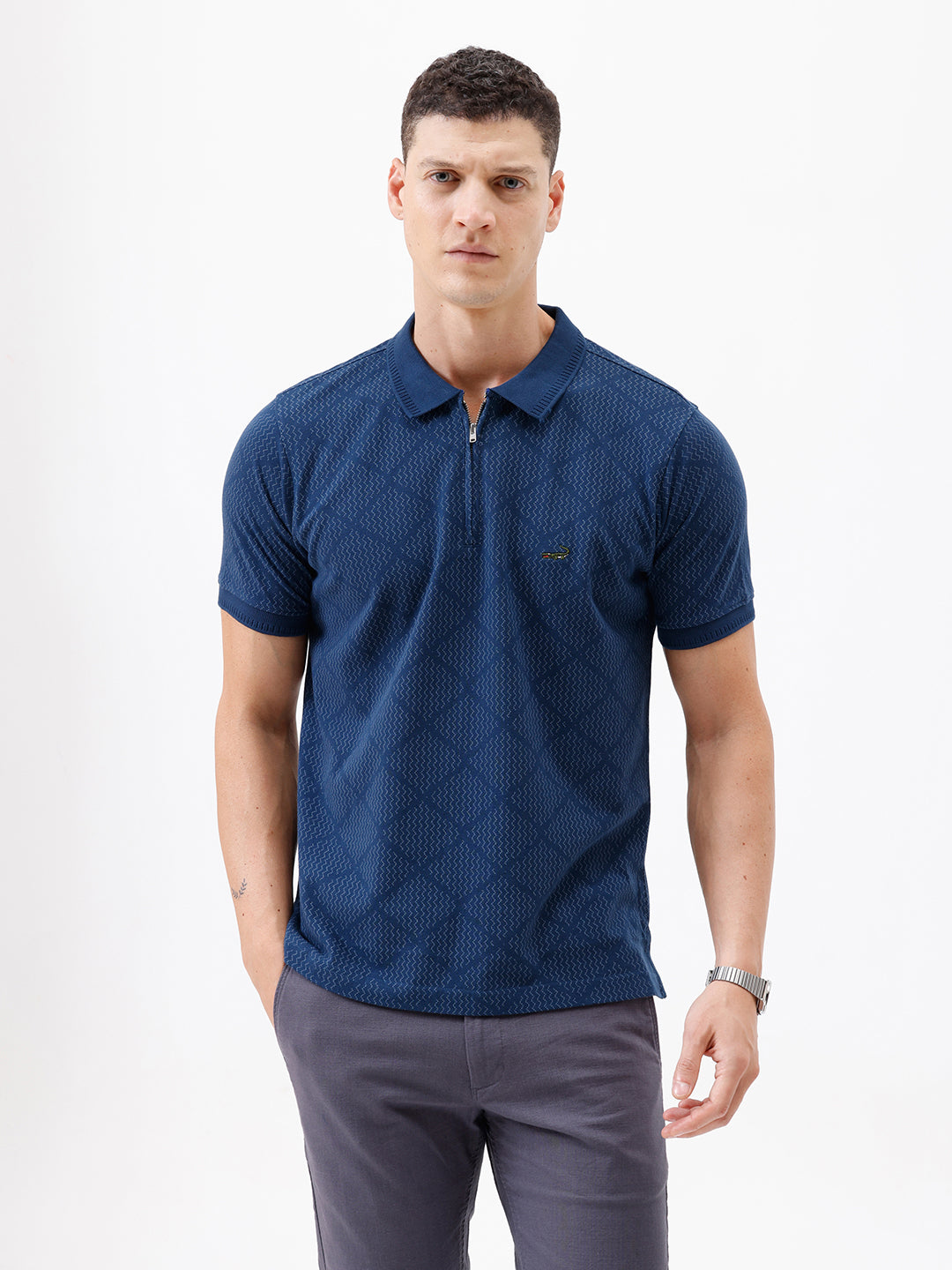 A man wearing a navy blue short-sleeve polo shirt with a subtle geometric pattern and a half-zip collar, paired with gray trousers, against a plain white background.