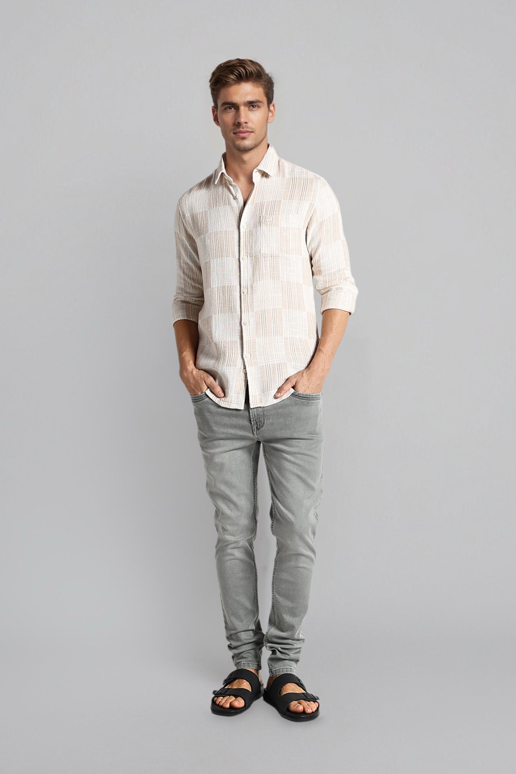 Man wearing a light-colored shirt and gray pants on a gray background