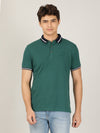 Man wearing a green green casual solid polo t shirt with casual styling on a gray background