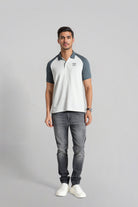 Man wearing a white and gray polo shirt with gray jeans on a light gray background