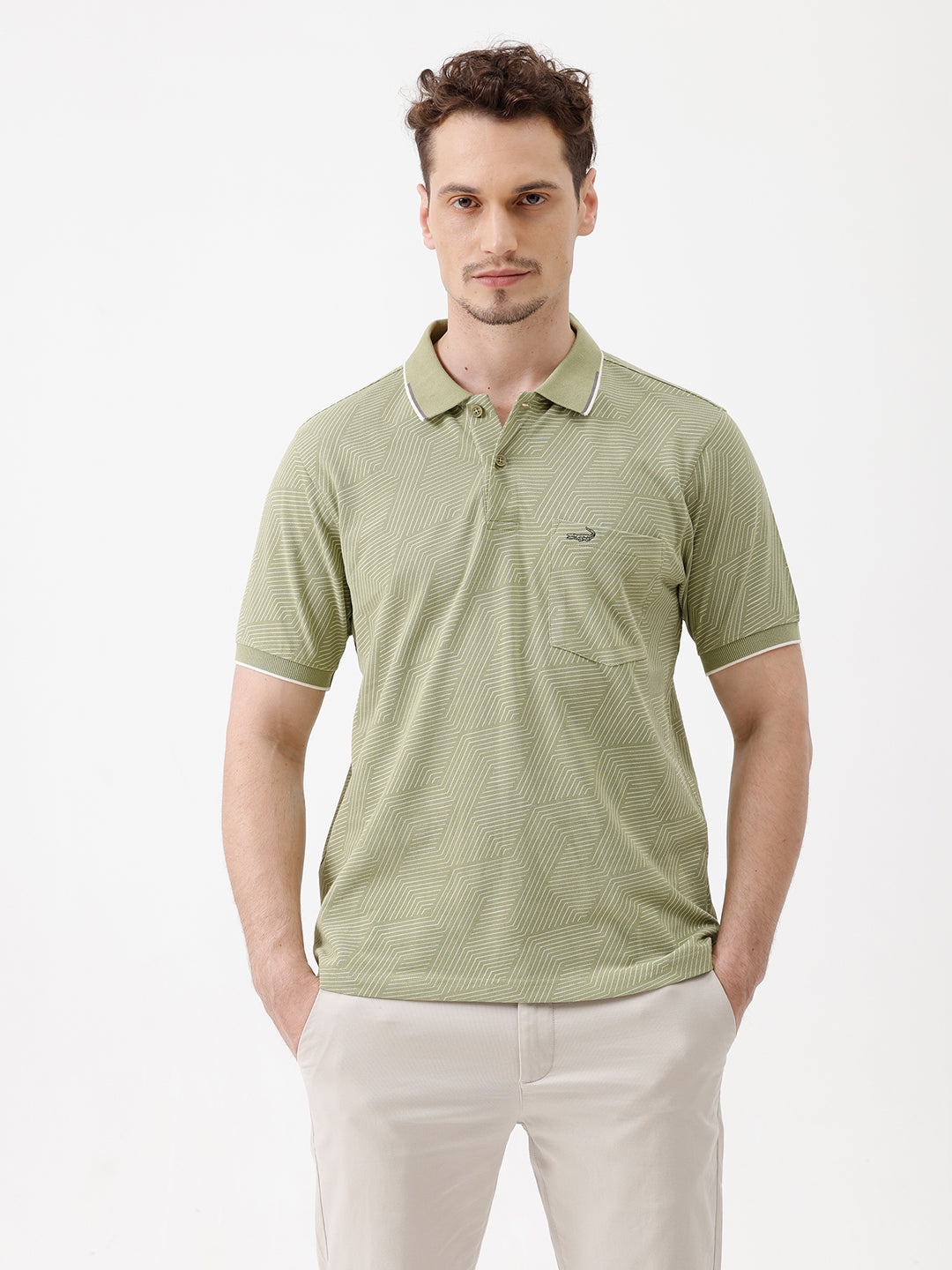 A man wearing a light sage green short-sleeve polo shirt with a subtle geometric pattern, paired with beige trousers, standing against a plain white studio background.