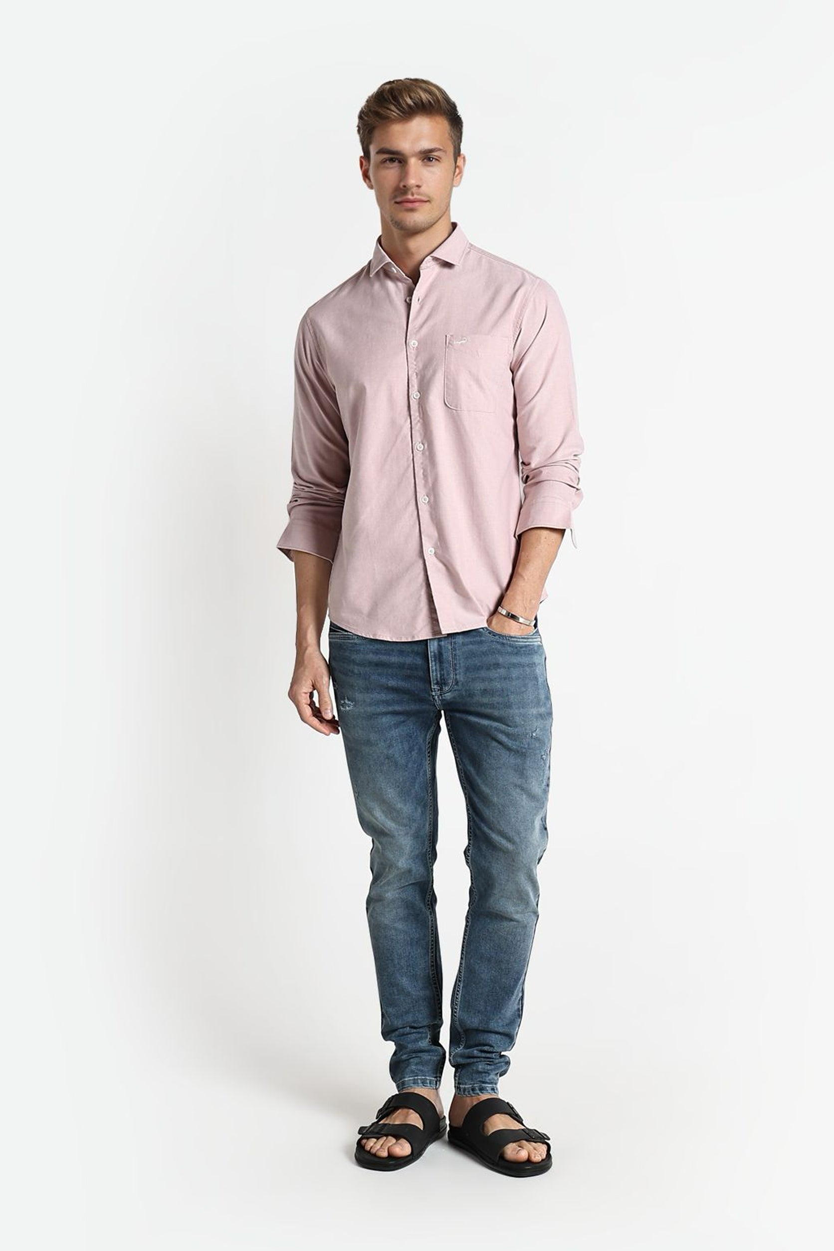 Man wearing a light pink shirt and blue jeans on a white background