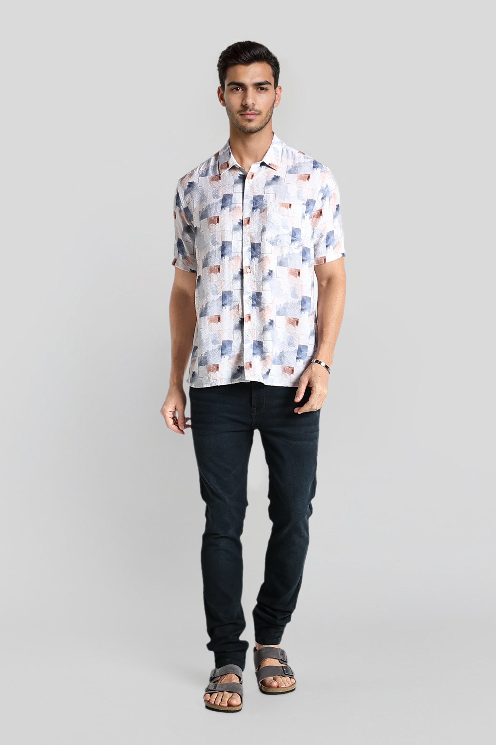 Man wearing a patterned shirt and dark jeans on a gray background