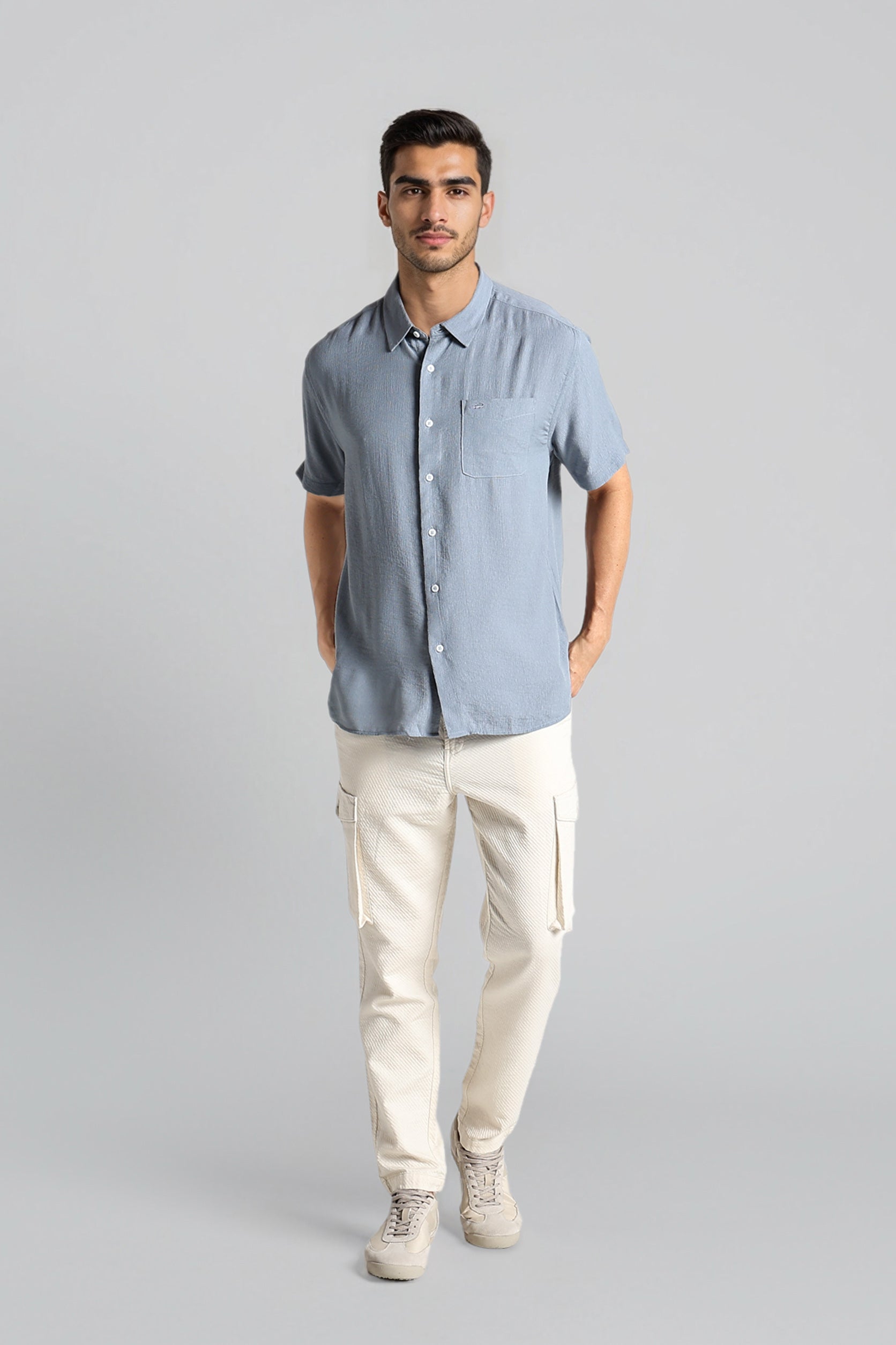 Man wearing a light blue button-up shirt and beige pants on a gray background