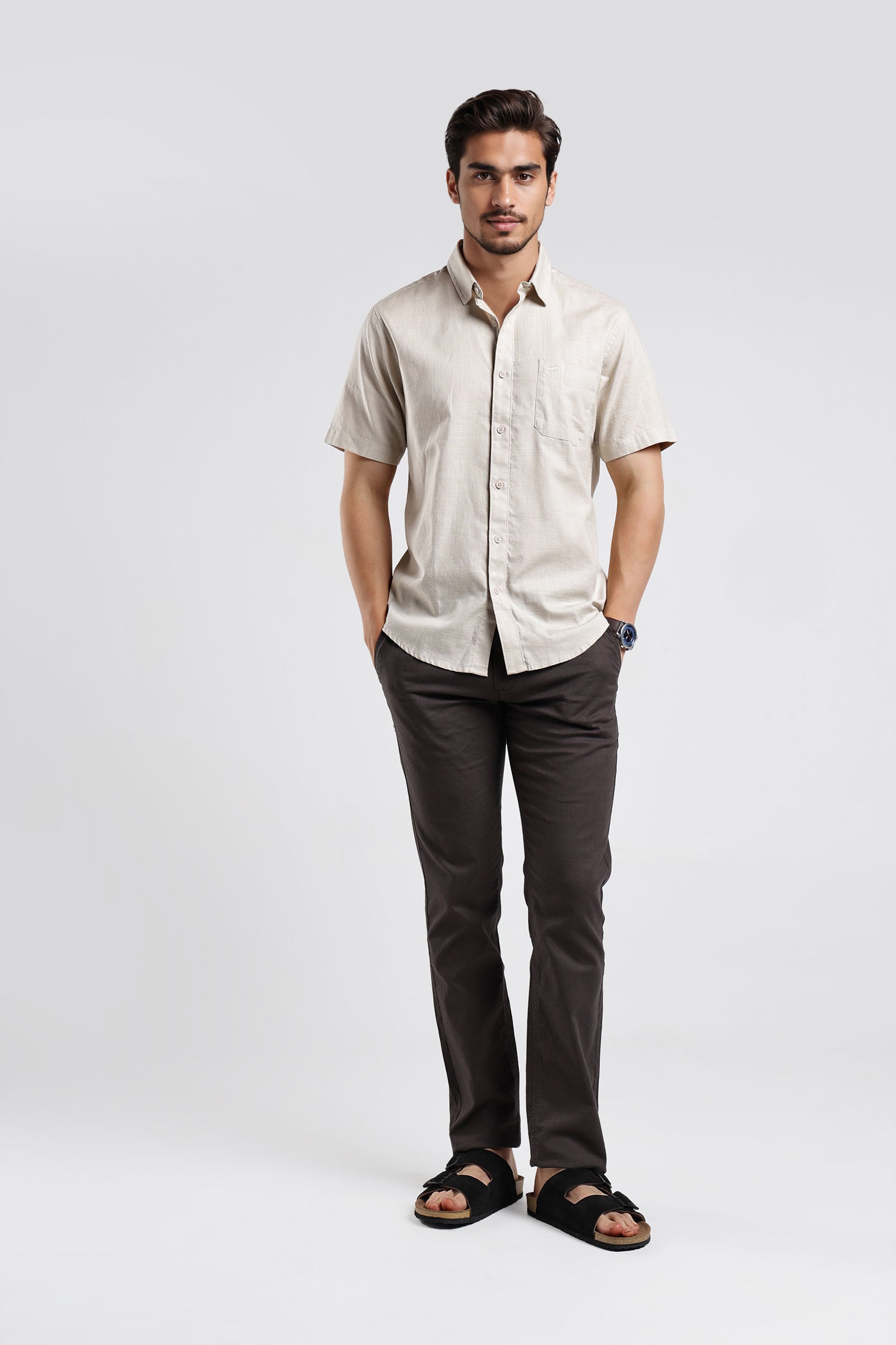Man wearing a beige shirt and dark pants on a white background