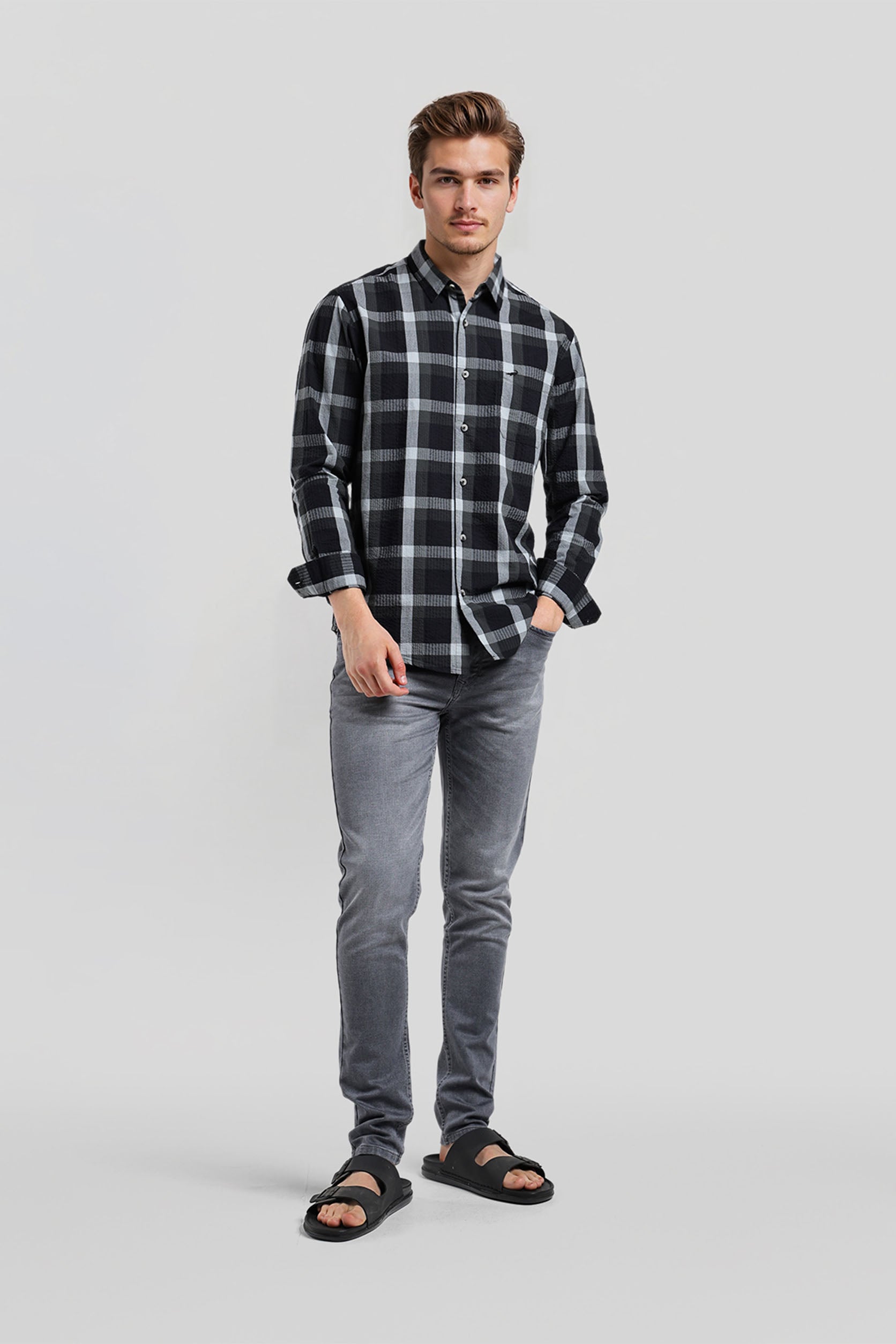 Man wearing a black and gray plaid shirt with gray jeans on a light gray background
