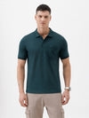 A man wearing a dark teal short-sleeve polo shirt with a chest pocket, paired with beige cargo pants, standing against a plain white studio background.