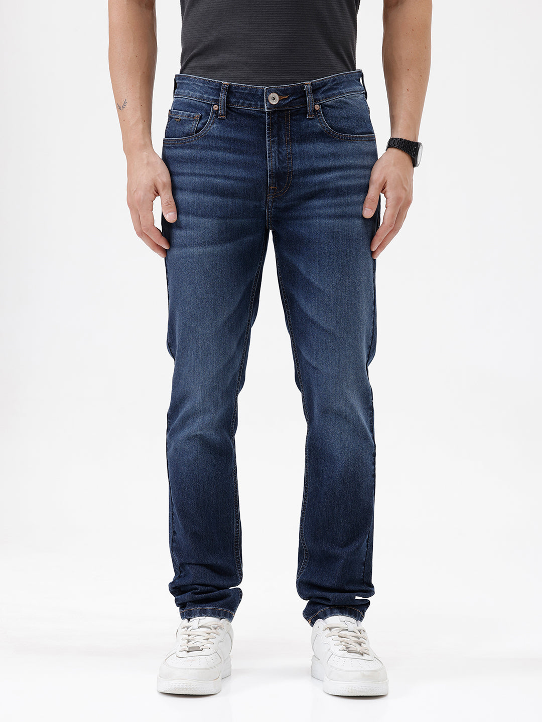 A person wearing dark blue slim-fit jeans with a faded wash, paired with a black t-shirt and white sneakers, shown from the waist down against a plain white studio background.