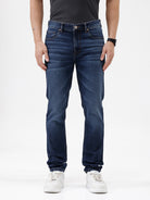 A person wearing dark blue slim-fit jeans with a faded wash, paired with a black t-shirt and white sneakers, shown from the waist down against a plain white studio background.