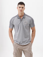 A man wearing a light gray short-sleeve polo shirt with darker gray shoulder panels and a small crest logo on the left chest, paired with khaki cargo pants, against a plain light gray studio background.