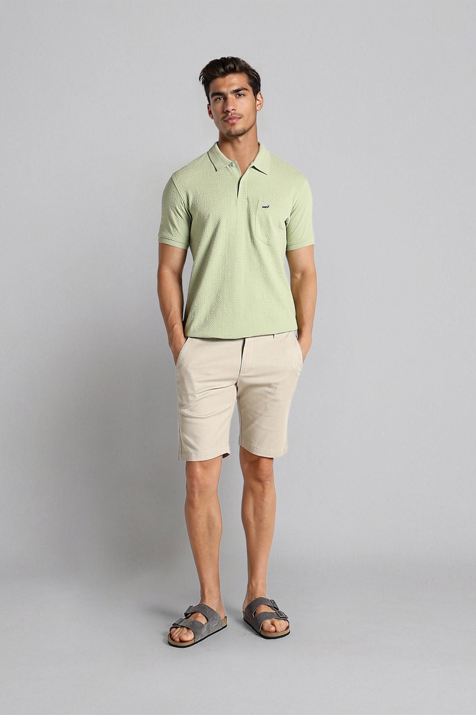 Man wearing a light green polo shirt and beige shorts on a gray background