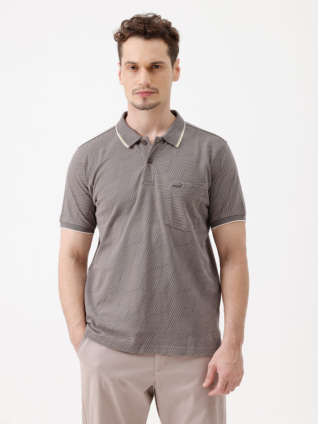 A man wearing a short-sleeve polo shirt with a gray and white geometric pattern, paired with beige trousers, standing against a plain white studio background.