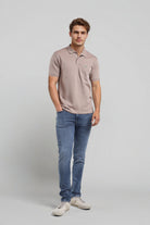 Man wearing a beige polo shirt and blue jeans on a light gray background