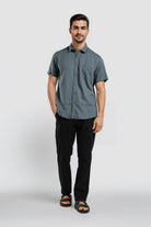 Man wearing a gray button-up shirt and black pants on a white background