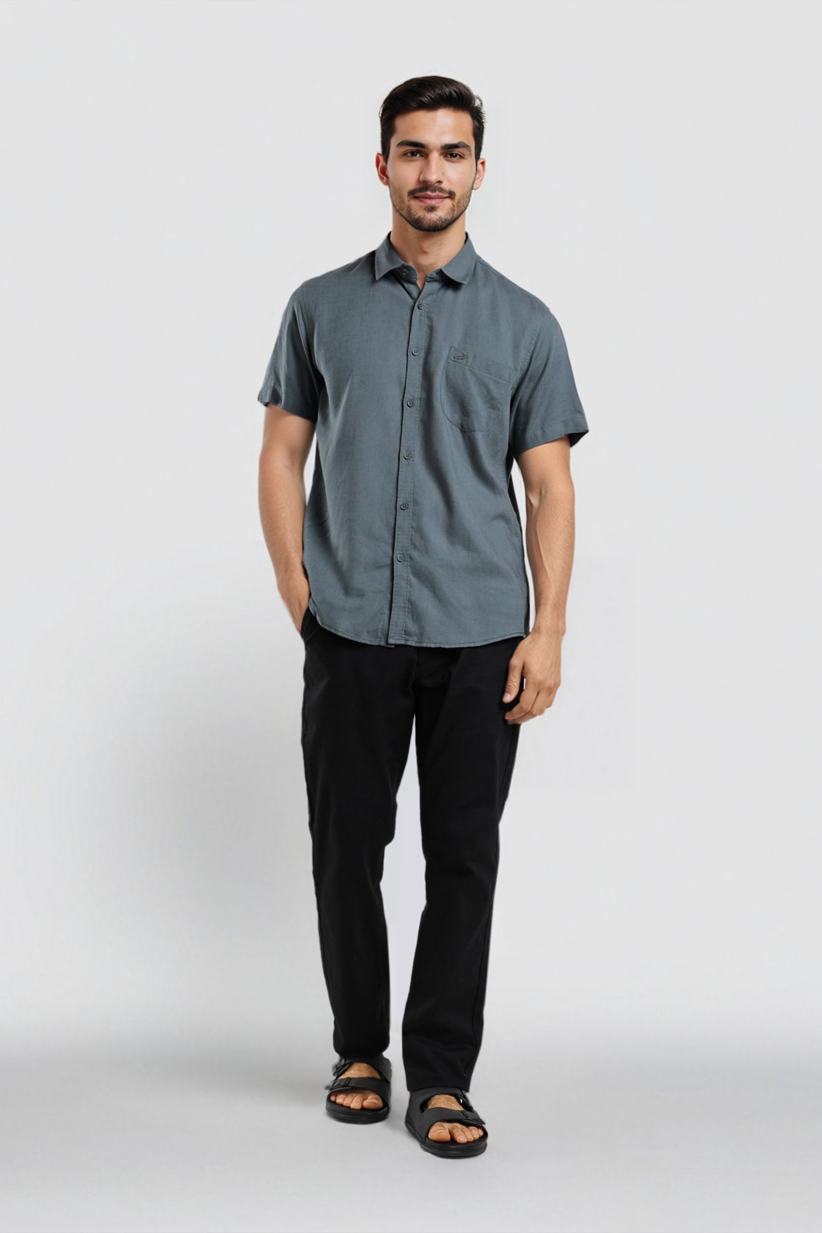 Man wearing a gray button-up shirt and black pants on a white background