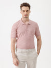 A man wearing a dusty pink short-sleeve polo shirt with a chest pocket, paired with light beige trousers, standing against a plain white studio background.