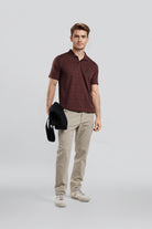 Man wearing a maroon polo shirt and beige pants holding a black jacket on a light gray background