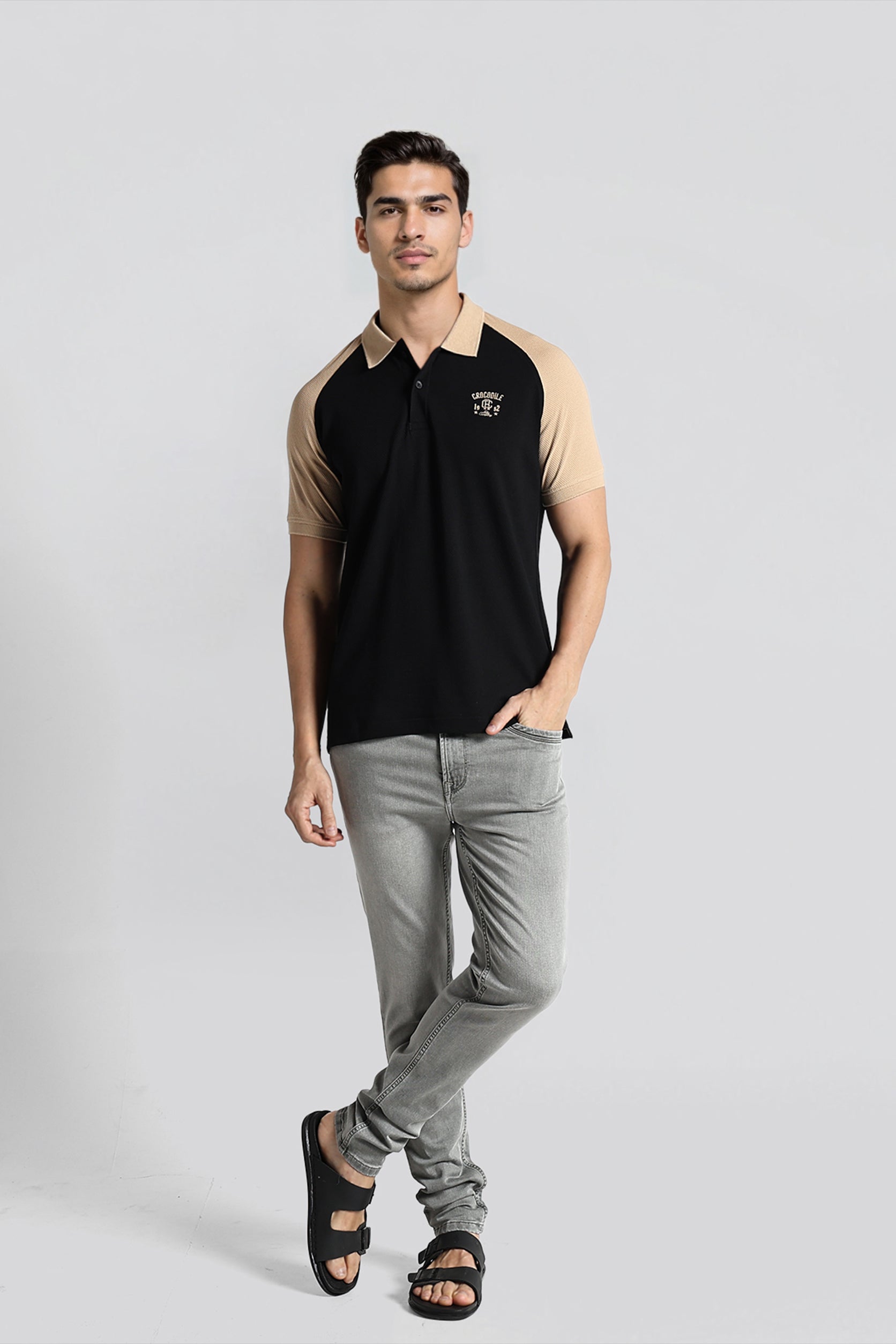 Man wearing a black and beige polo shirt with gray jeans on a white background