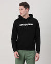 Man wearing a black solid black hoodie with casual styling on a gray background
