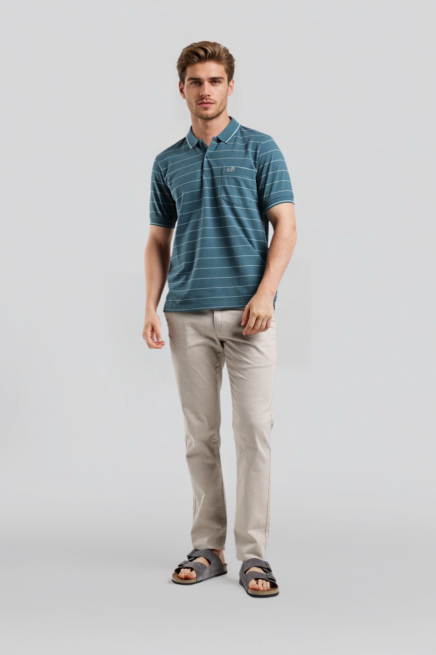 Man wearing a blue striped polo shirt and beige pants on a light gray background